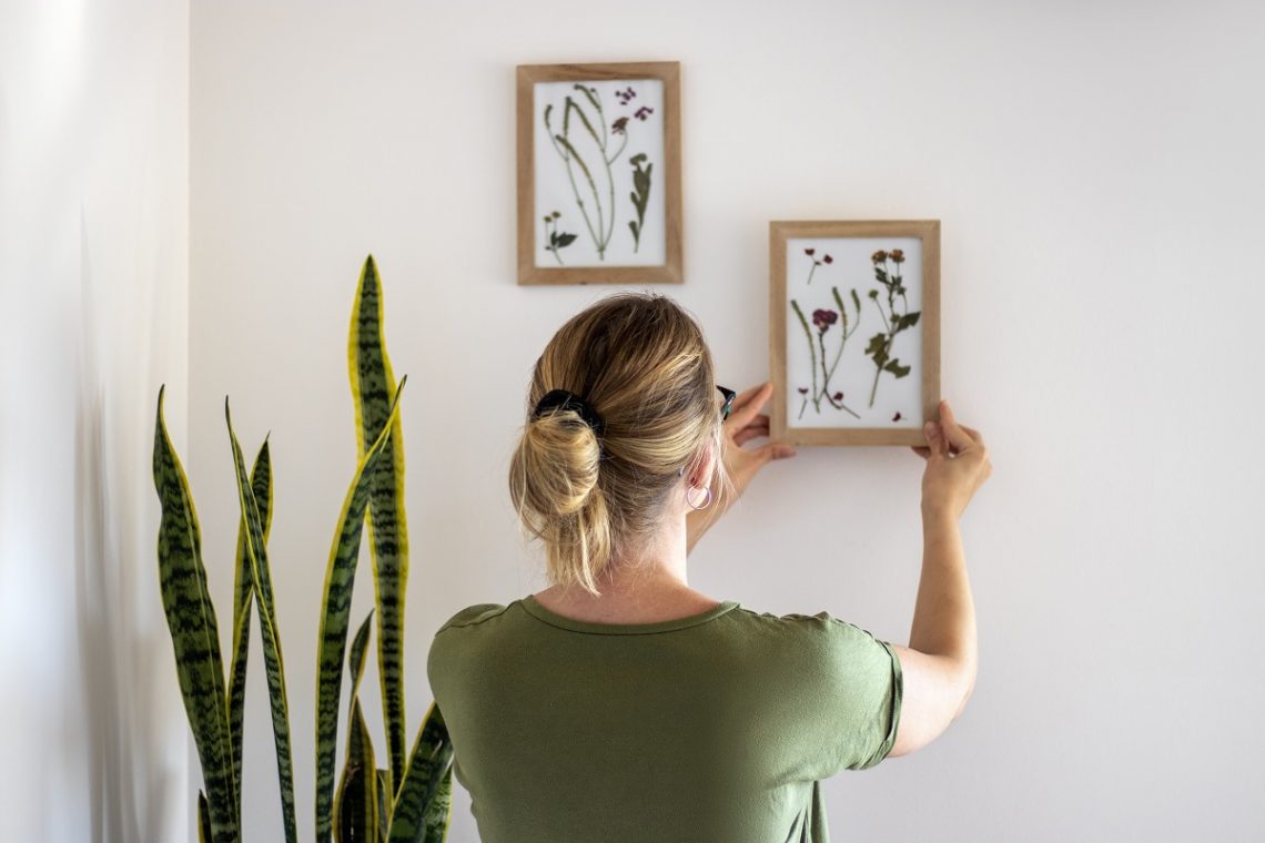 woman hanging framed pressed flower art on the wall