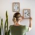 woman hanging framed pressed flower art on the wall