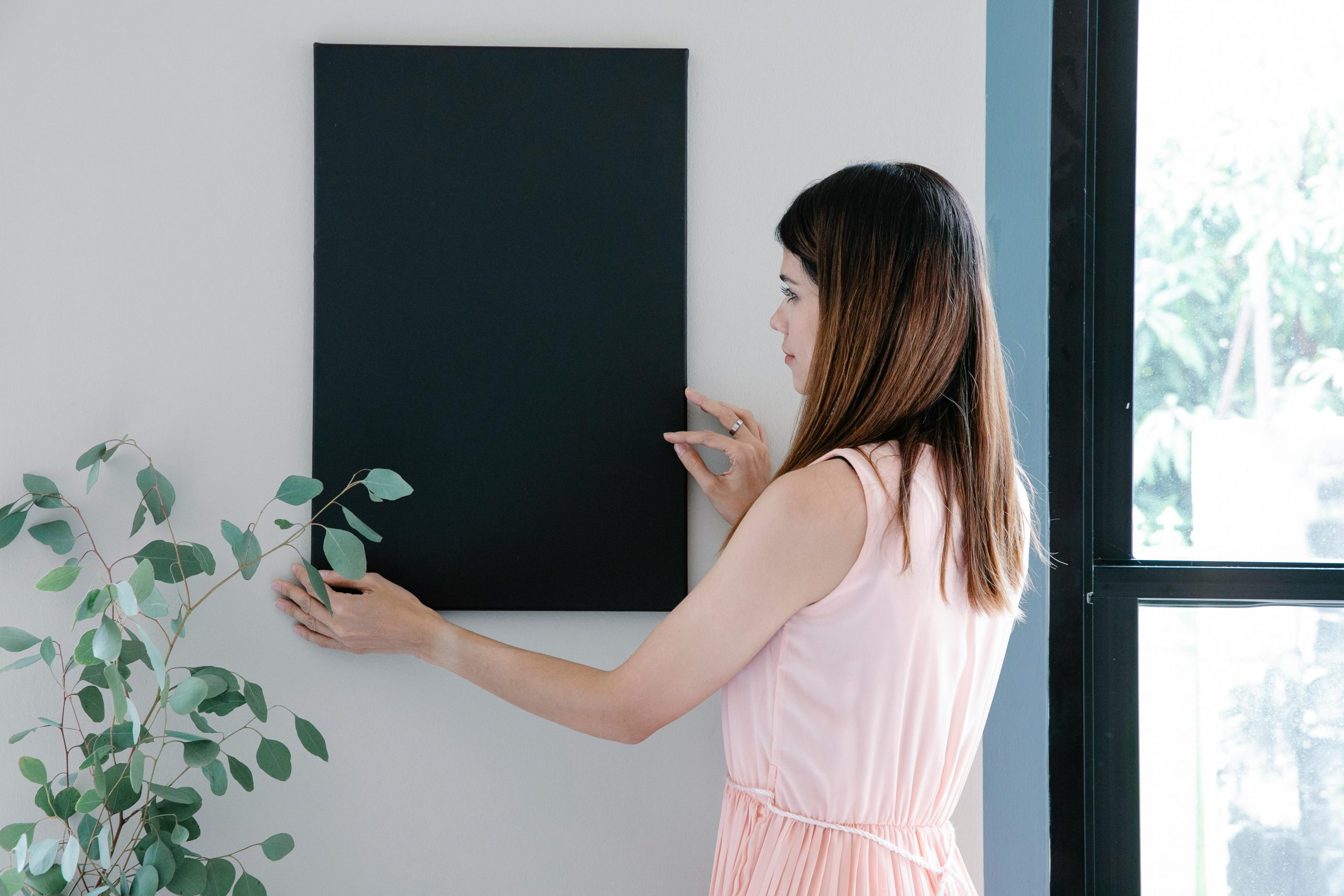 woman hanging a picture on the wall beside a window