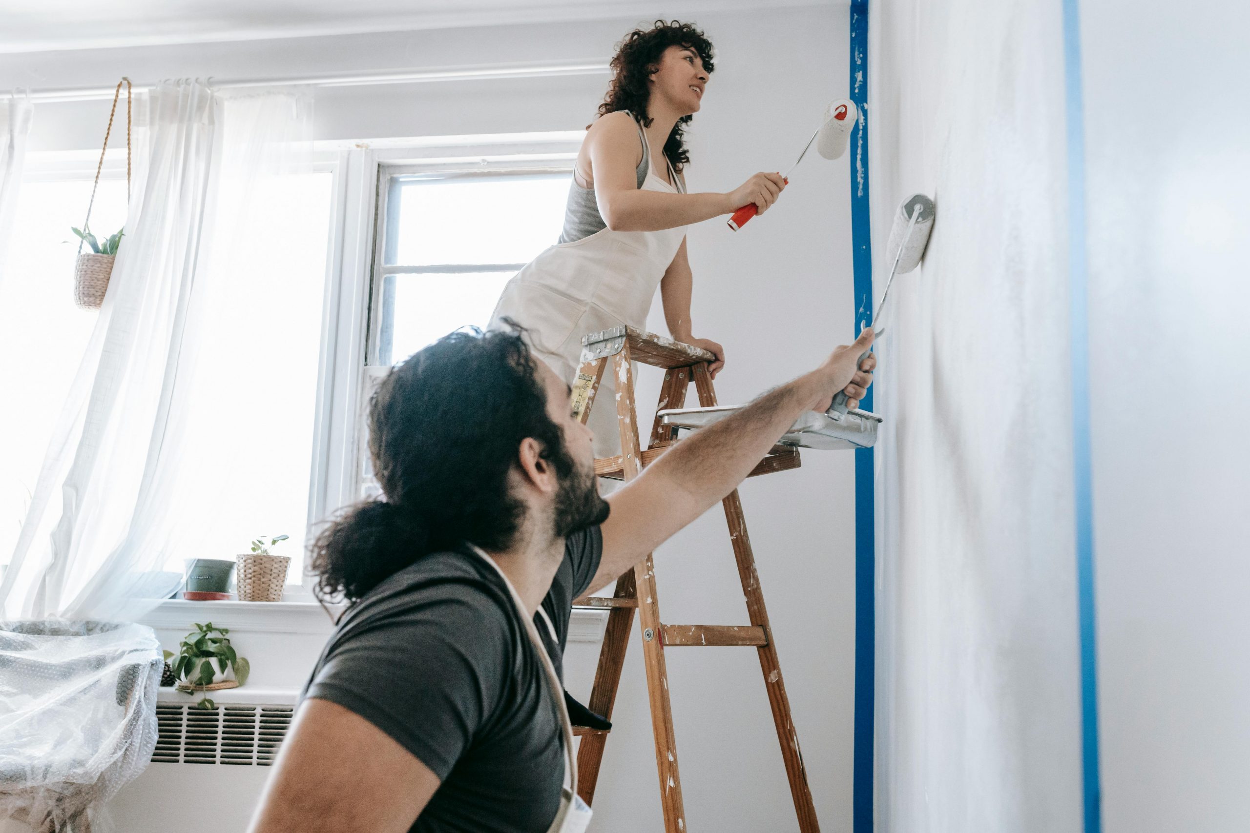 couple painting the interior walls of a room white using paint rollers