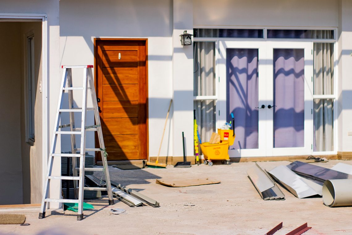 freshly painted house exterior with a ladder leaning against the wall and various construction materials scattered