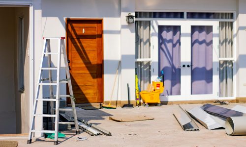 freshly painted house exterior with a ladder leaning against the wall and various construction materials scattered