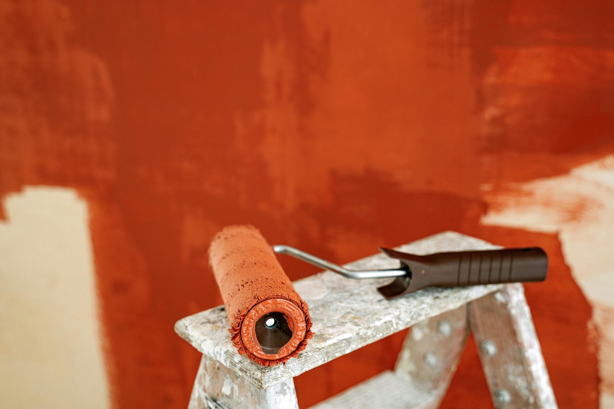 orange paint roller on a ladder, with an orange wall in the background